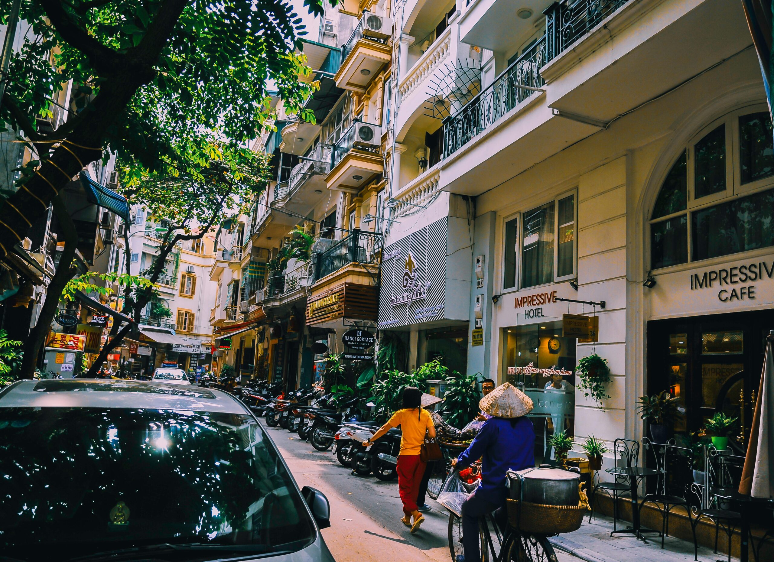 Vibrant street life in Hanoi with locals, cafes, and motorbikes on a sunny day.