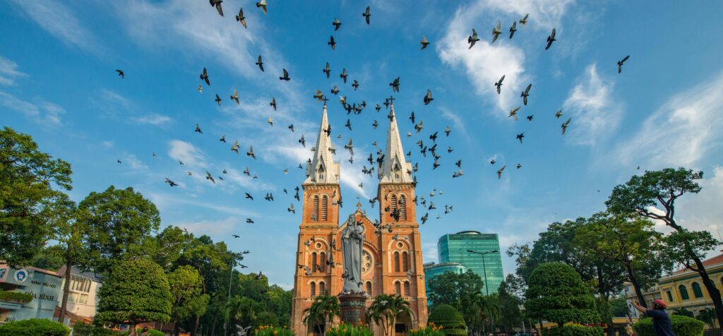 Flock of birds flying over Notre-Dame Cathedral Basilica Saigon in vibrant daylight.