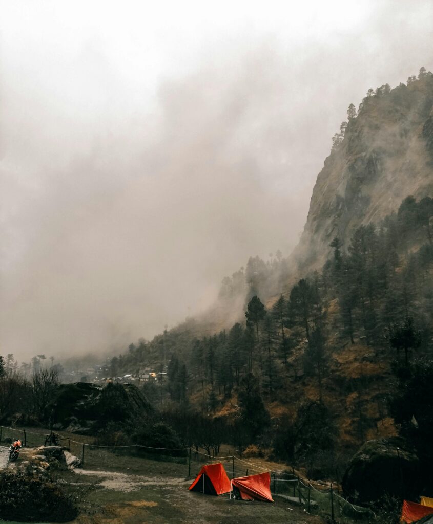 Misty mountainside with red tents at a campsite in Kasol, India, creating a serene outdoor scene.
